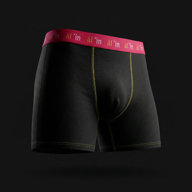Black boxer briefs with a red waistband on a black background